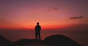 In a red sunset, a man takes a selfie on a cliff in bright red sky. 
Nature video High quality footage. Meditation ocean and sky background. 
Majestic sunset or sunrise cloudscape background.