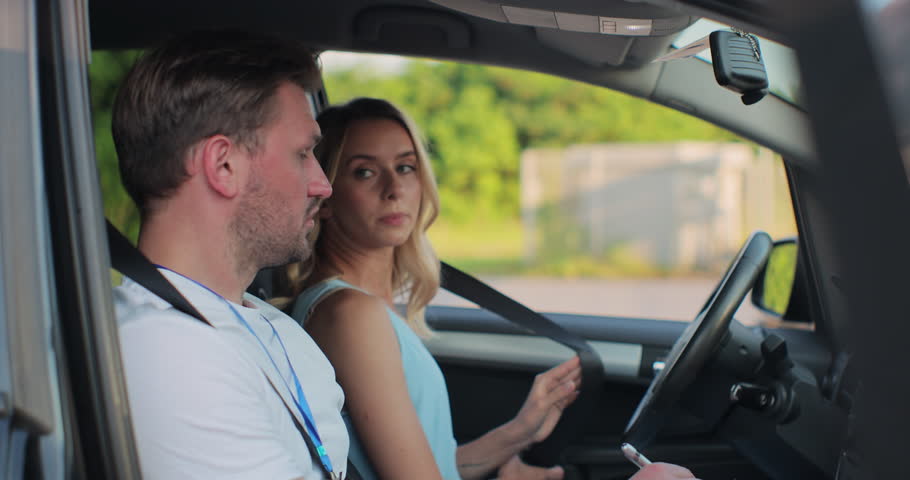 Young woman and driving school instructor with clipboard talking in car. Woman listening to instructor in car learning to drive. Royalty-Free Stock Footage #1107937259