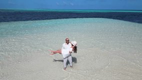Top aerial drone view of the dancing couple by the ocean in the Maldives, in white clothes, a man gently takes the woman in his arms and spins her, their movements echoing the rhythm of the ocean wave
