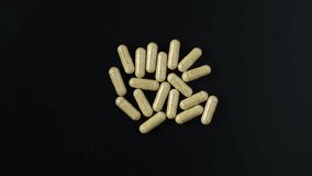 Hulbah pills or Fenugreek capsules on dark background, top view. 4K video, Rotating. Nutritional supplement. Natural vitamins. Herbal medicine concept.