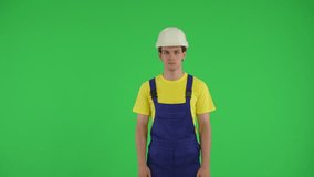 Medium green screen isolated chroma key video of a young construction worker looking at the top of the frame and pointing at it.