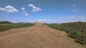 Drone video flies to a sword monument on a hill, passing a field and a country road. A clear blue sky serves as the backdrop. Great for travel and history-themed videos.
