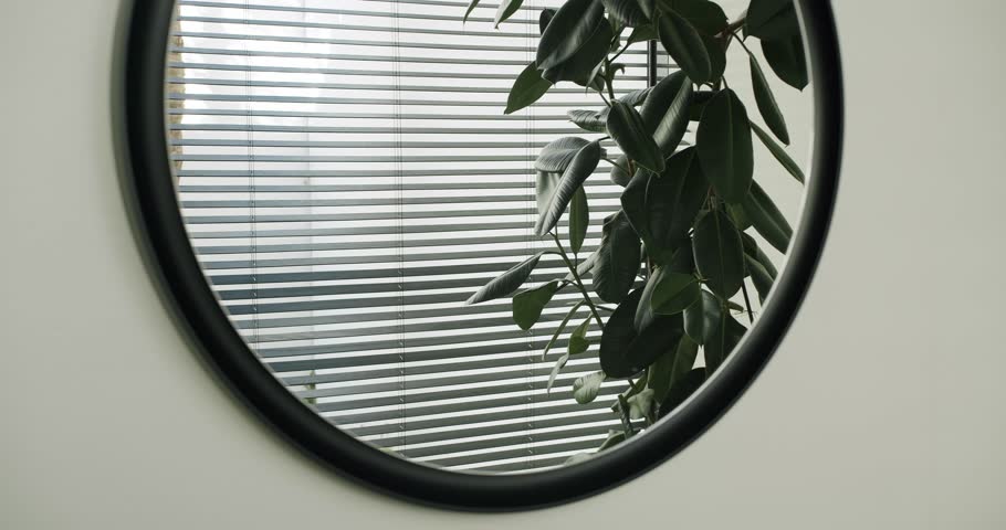 Closeup of mirror in black frame hanging on white wall in bathroom with modern interior. 