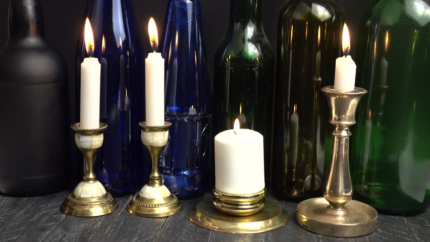 Burning white candles in old vintage brass and bronze candlesticks against the background of glass multicolored bottles - Powered by Shutterstock - Get 15% off with code: PIKWIZARD15