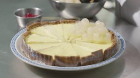 Close up of a chef's hand wearing black gloves laying an longan on top of a pie. Decorate the cake. The process of making an pie dessert at home in the kitchen. Bakery