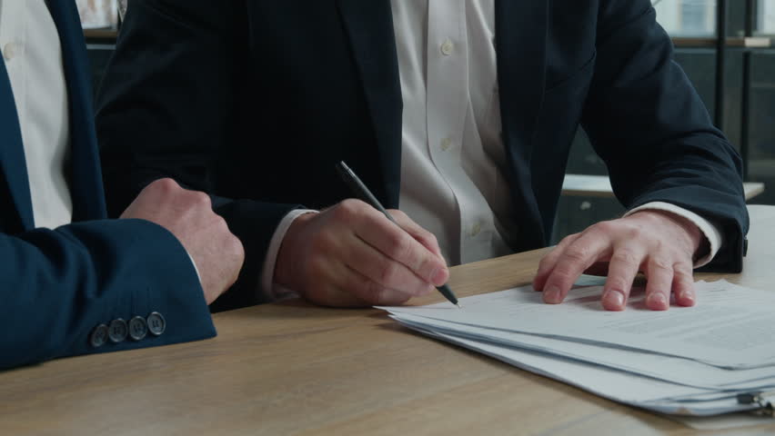 Close-up two unrecognizable businessmen men business partners signing contract document conclude successful financial deal at meeting in office sign for partnership cooperation shake hands handshake