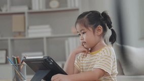 Asian girl looking and touch on white screen at the tablet screen attentively. overstimulated children concept. Too much screen time. Cute girl watching videos while tv, Internet addiction concept.
