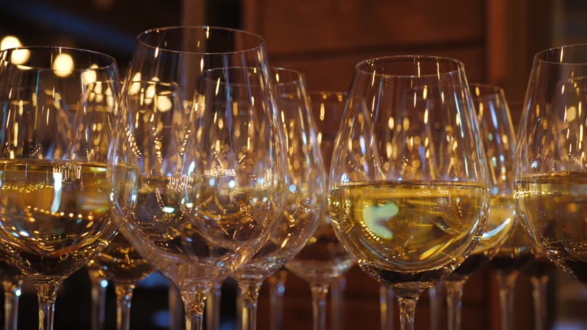 Shiny luxurious glasses of white wine on a buffet table at an event beautifully lined up in warm evening light with blurry lights close-up