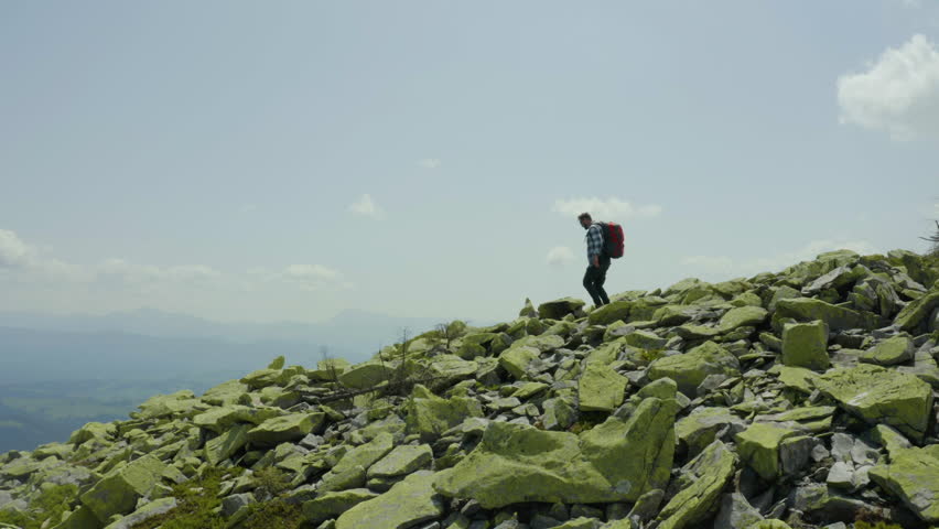 A man walks along a mountain slope covered with giant stones. Solo tourism. Hard hike, adventure tourism concept.