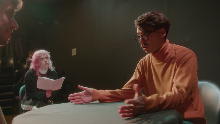 Talented actor sitting behind the table on theater stage and talking emotionally to partner, female dramaturg commenting on performance during rehearsal
