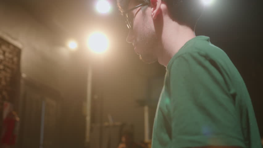 Young male stage director holding play script and watching two actors holding hands and having romantic dialogue while rehearsing love scene before theater performance