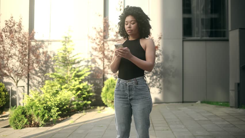 Portrait of nervous unhappy young african american woman feeling annoyed when getting message on her phone at city street Annoyed curly female having problem conflict by smartphone outdoors Royalty-Free Stock Footage #1107956151