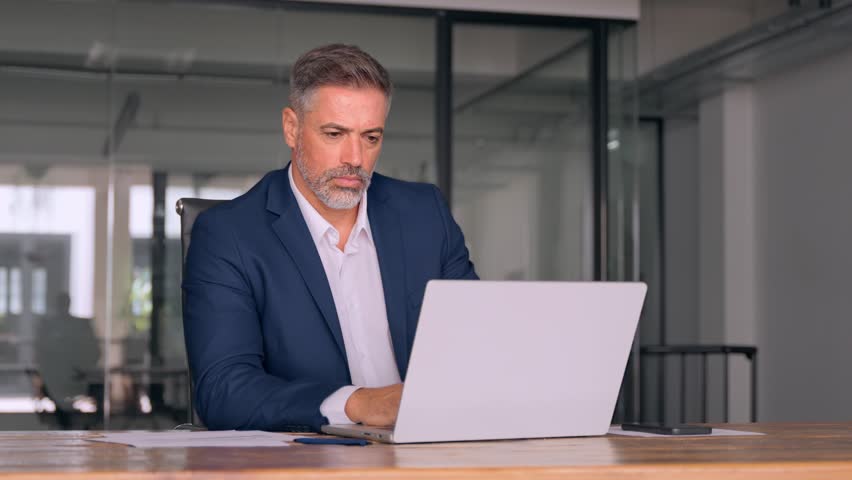 Mature Indian or Latin business man ceo trader using computer, typing, working in modern office, doing online data market analysis, thinking planning tech strategy looking at laptop with copy space. Royalty-Free Stock Footage #1107956617