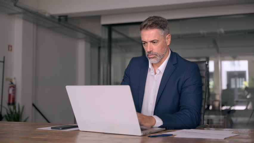 Portrait of mature Indian or Latin business man ceo trader using laptop computer, typing, working in modern office. Middle-age Hispanic smiling handsome businessman entrepreneur looking at laptop. Royalty-Free Stock Footage #1107956629