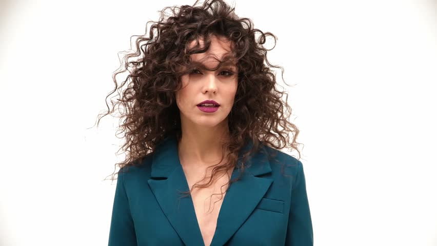 Beautiful brown-haired girl with a perfectly curly flying hair, classic make-up and a blue suit. Beauty face and hair.