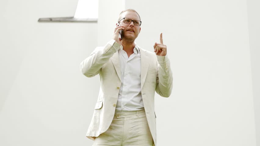 Young Man in White Suit Talking Angry and Upset on Mobile Phone Outside Arguing