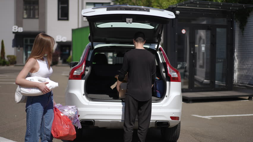 Live camera follows young couple walking from car to recycling station in urban city. Tracking shot of Caucasian confident man and woman separating garbage strolling with trash outdoors