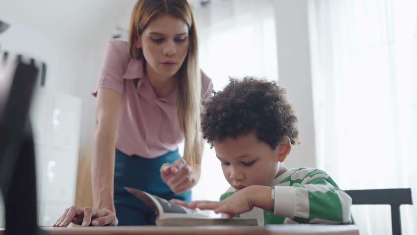 Female teacher helping little African American boy reading a book at school. kindergarten woman teacher talking and explaining with little school boy reading a book. Education and learning concept Royalty-Free Stock Footage #1107968527