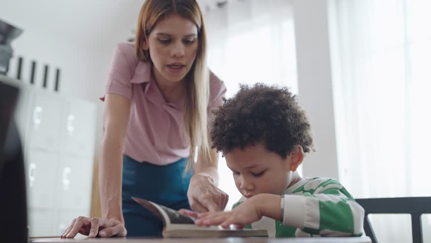 Female teacher helping little African American boy reading a book at school. kindergarten woman teacher talking and explaining with little school boy reading a book. Education and learning concept - Powered by Shutterstock - Get 15% off with code: PIKWIZARD15