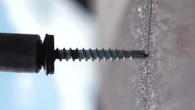 Screwing a roofing screw into a metal tile. Close-up of fastening a metal tile with screws. Roof installation.vertical video screen