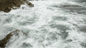 Rocks in the sea of Spain at a strong wind. White splashing waves crash against the shore. sunny spring day. Rocks in the sea of Spain at a strong wind. White splashing waves crash against the shore