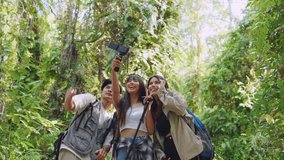Group of Asian backpacker vlogger have fun travel in forest together. Attractive man and woman friends traveler use camera record video vlog, walk in nature wood with happiness during holiday vacation