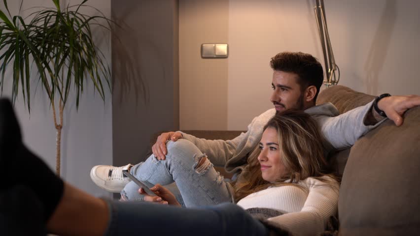 A Caucasian couple sitting on the sofa watching TV in the romantic mode of their home, lifestyle of a couple on a romantic evening. 4k video