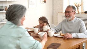 Caucasian couple in love spending time with cute grandchild talking about family relationship during breakfast time in dining room, granny people during morning routine with child - Powered by Shutterstock - Get 15% off with code: PIKWIZARD15
