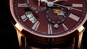 Extreme closeup of  second arrow passing by on clock face. Lengthwise view of luxury swiss watch. Running second arrow. day and night indicator on the watch face. burgundy watch face