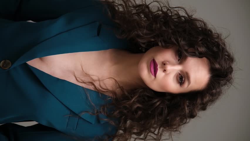 Beautiful brown-haired girl with a perfectly curly flying hair, classic make-up and a blue suit. Beauty face and hair.