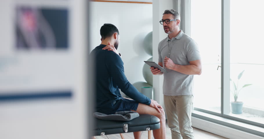 Physiotherapist, man and consultation for joint pain with tablet and medical support in a physical therapy clinic or rehabilitation. Physio, doctor and consulting person or advice for healing injury Royalty-Free Stock Footage #1108000455