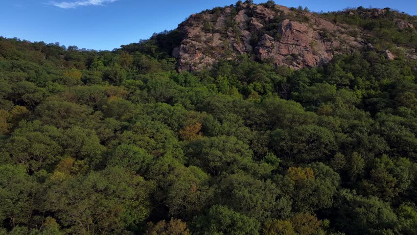 An aerial view of the peaceful scenery of Storm King Mountain in upstate New York on a beautiful day. The drone camera dolly in, boom up and tilt up towards the mountain peak and white clouds.