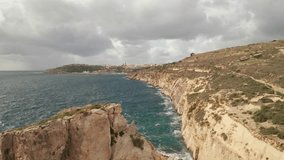 Aerial reverse flying drone shot capturing Gozo's rugged coast, the drone reveals the intricate details of the rocky formations below, juxtaposed against the lively turquoise sea. LuPa Creative