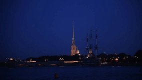 Side view from tour boat of illuminated Russian Orthodox Saints Peter and Paul Cathedral above Trinity bridge at night in Saint Petersburg city, Russia. Real time handheld video. Water travel theme.