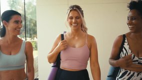 Three mature female friends wearing fitness clothing carrying exercise mats and chatting at gym or yoga class - shot in slow motion - Powered by Shutterstock - Get 15% off with code: PIKWIZARD15