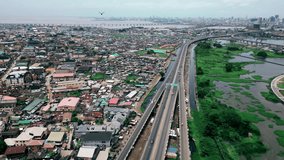 The drone is flying up and backwards high above the highway with lots of houses in a residential area on the left in Lagos Nigeria Aerial Footage 4K