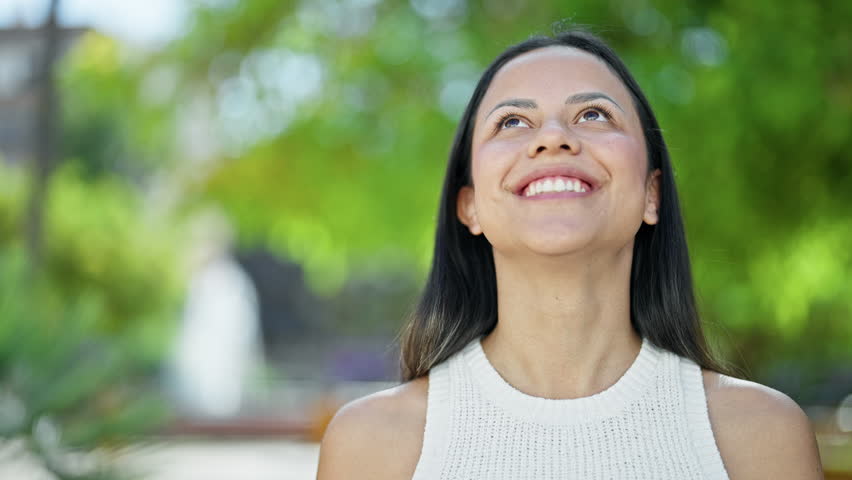 Young beautiful hispanic woman looking to the sky with winner expression at park