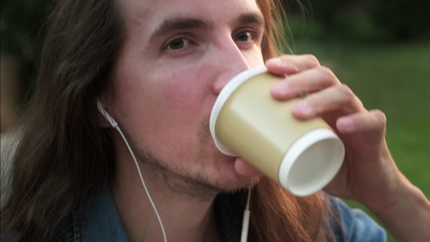 Young man with headphones smoking e-cigarette and drinking coffee outdoor at evening | Shutterstock HD Video #1108025677