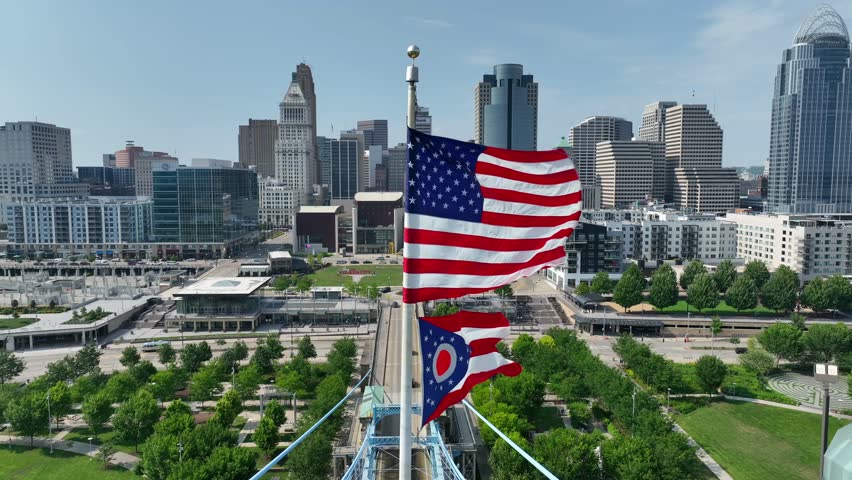 Cincinnati skyline with American and Ohio flags waving on John A. Roebling Suspension Bridge. Aerial establishing shot of a beautiful American city during summer.