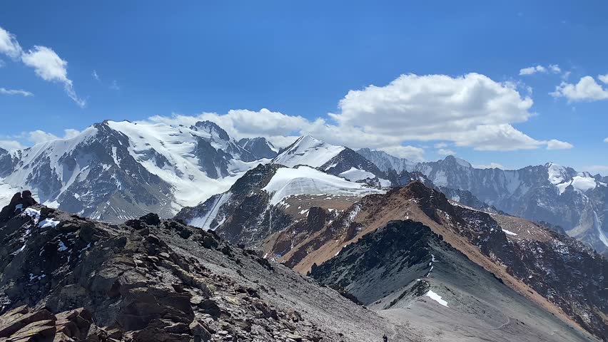 Fascinating view from the top of Komsomolets Peak mountain. Ala-Archa National Park, Kyrgyzstan. Snow-capped mountains, rocks, slopes and peaks of the Kyrgyz ridge.