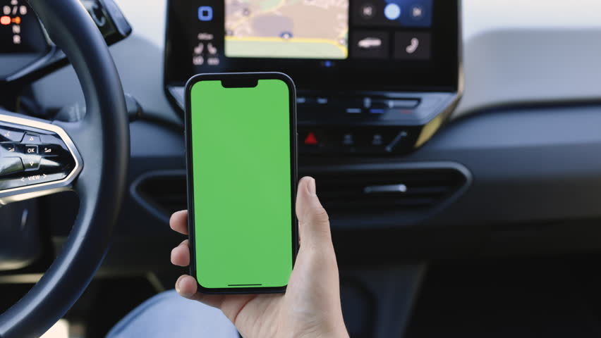 The green screen of the phone is chroma key in the car. Driver is sitting in the car and watching her smartphone with green screen at day. Man holding mobile phone on the background of a car interior. Royalty-Free Stock Footage #1108035397