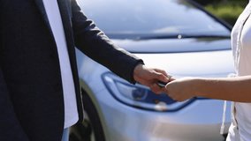 Man giving keys of car to buyer. Unrecognized people shaking hands in electric car dealership on background of bought cars. Businessman giving car key to woman in automotive dealership showroom - Powered by Shutterstock - Get 15% off with code: PIKWIZARD15
