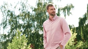 Handsome smiling stylish hipster lambersexual model. Modern man dressed in pink shirt and trousers. Fashion male posing in the street background. Outdoors