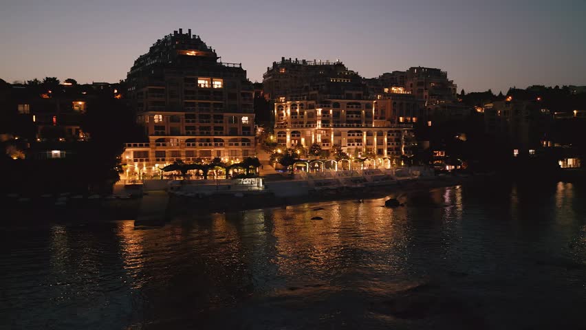 At night, a drone unveils a luxurious seaside hotel on Bulgaria's coast. Lights craft a magical ambiance of warmth and luxury. Royalty-Free Stock Footage #1108039707