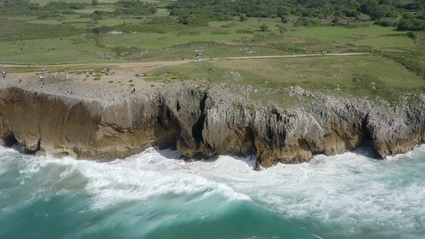 Aerial parallax around crashing waves on rocky limestone cliffs, bufones de pria asturias spain, slow motion