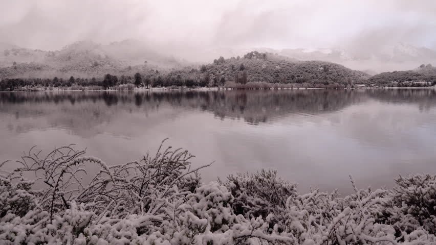Magical view of the calm lake, forest and mountains in winter at sunset. Beautiful landscape reflection in the water surface. The snow covers the plants.
