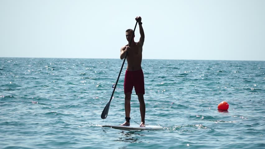 Man Sup Sea. Strong athletic man learns to paddle sup standing on board in open sea ocean on sunny day. Summer holiday vacation and travel concept. Aerial view. Slow motion