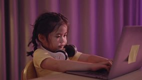 Asian girl smiling, laughing, excited, looking, wearing white headphone and using laptop streaming night light in living room at home. Cute girl watching videos while tv Internet addiction concept.