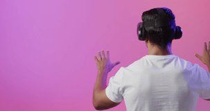 Video of biracial man using vr headset on pink and purple background. Technology, global connections and communication metaverse.
