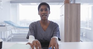 African american female doctor holding medication and making video call in hospital, slow motion. Medical services, healthcare, telemedicine, communication and medicine, unaltered.